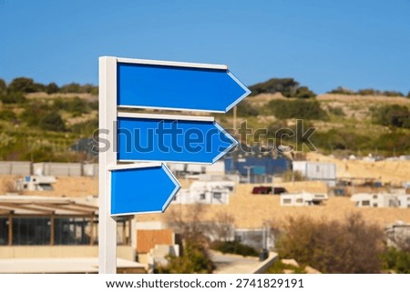 Set of three empty blue arrow signs on white metal pole against defocused sunny beach under clear sky. Space for text, close up.