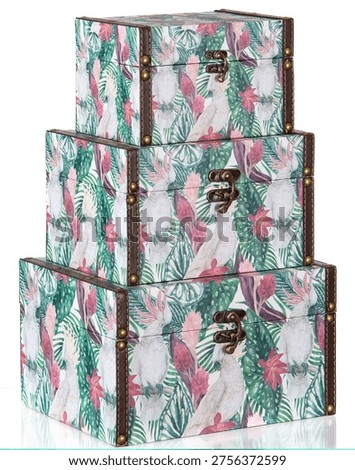 Set of three stacked decorative boxes with a tropical print of green leaves and white birds. They feature brown leather details and metal clasps, combining vintage and elegant style.