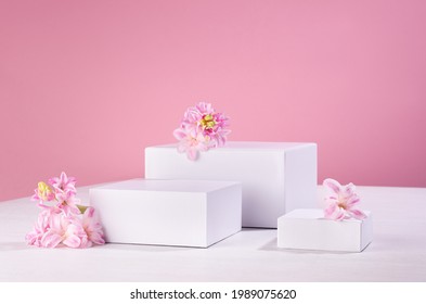 Set Of Three White Podiums For Presentation Cosmetics Produce With Fresh Spring Flowers On Pastel Pink Background.