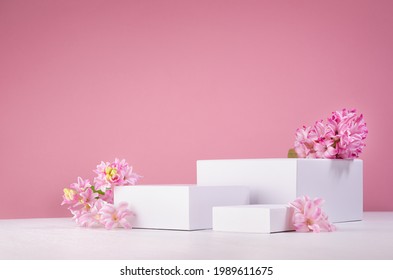 Set Of Three White Podiums For Presentation Cosmetics Produce With Fresh Spring Flowers On Pastel Pink Background.
