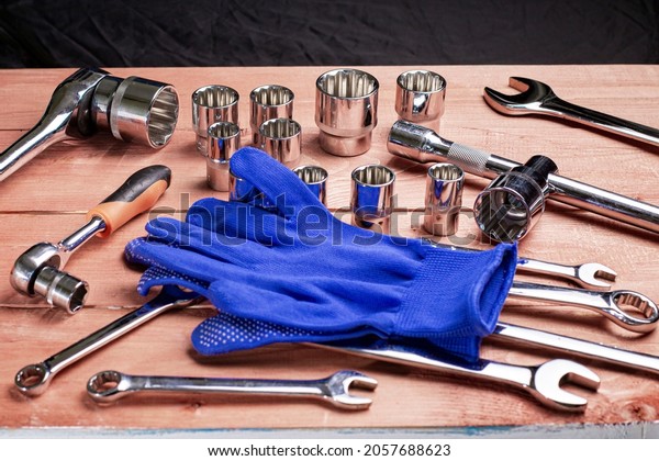 A set of tools and wrenches with work gloves on a\
wooden work table.