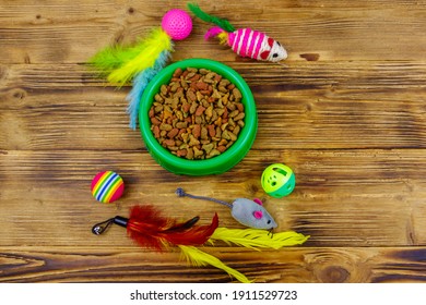 Set Of Toys For Cat And Bowl With Dry Pet Food On Wooden Background. Pet Care Concept