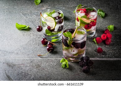 Set of traditional summer refreshing drinks berry mojito. With lime, mint leaves, blackberries, raspberries and cherries. With the ingredients on a dark stone table. Copy space