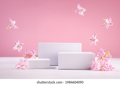 Set Of Tree White Podiums For Presentation Cosmetics Produce With  Flying Fresh Spring Flowers  On Pastel Pink Background.