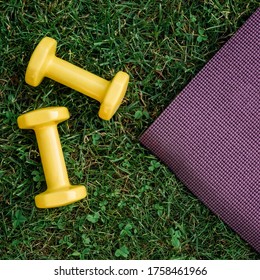 Set of two  yellow dumbbells and purple rubber Mat on a green grass background, top view. Staying in shape. Fitness and shape. Female exercise gear. Сoncept of outdoor fitness, nobody. - Powered by Shutterstock