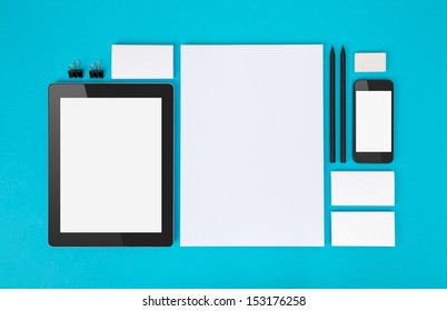 Set of variety blank office objects organized for company presentation or branding identity with blank modern devices. Isolated on blue paper background.