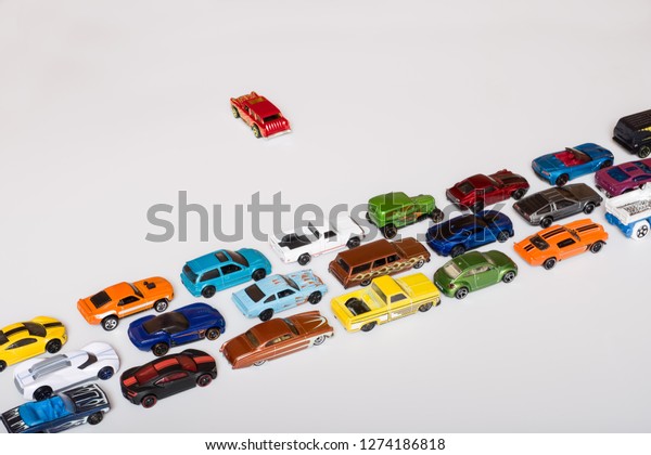 Set of various cars toys toy cars on\
white table. All go one way and one to the\
other.