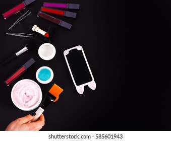 Set Of Various Cosmetics: Cream, Gel, Lipsticks, Lip Gloss, Brushes, Powder Puff, Tweezers, Cell Phone And Brush In Hands Isolated On Black Background, Copy Space, Top View