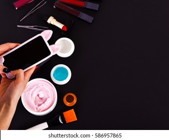 Set Of Various Cosmetics: Cream, Gel, Lipsticks, Lip Gloss, Brush, Tweezers And Cell Phone In Hands Isolated On Black Background, Copy Space, Top View