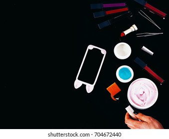 Set Of Various Cosmetics: Cream, Gel, Lipsticks, Lip Gloss, Brushes, Powder Puff, Tweezers, Cell Phone And Brush In Hands Isolated On Black Background, Copy Space, Top View