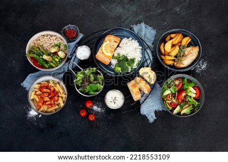 Set of various main dishes. Different healthy main courses, meat and fish dishes, pasta, salads, sauces, bread and vegetables on a dark background. Top view.
