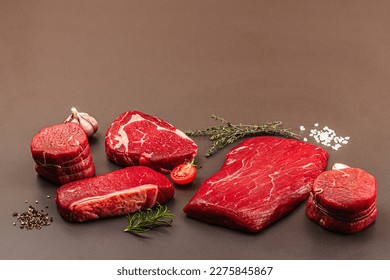 Set of various steaks with classic spices and herbs. Fresh raw meat cuts includes ribeye, eye round, flank and striploin steaks. Black stone concrete background, flat lay, copy space - Shutterstock ID 2275845867