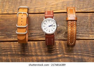 A Set Of Watches And Handmade Leather Straps For Them. Stylish, Vintage Replacement Watch Straps Made Of Natural Skin, Leather Brown And Cognac Color And Watches On A Wooden Background.