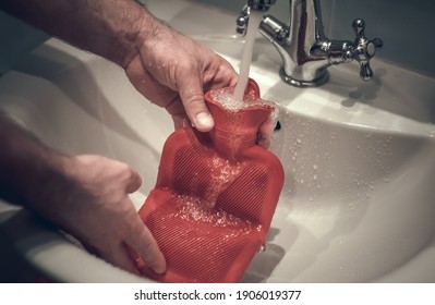 A Set Of Water In A Hot Water Bottle Under The Tap In The Sink. Men's Hands Hold A Rubber Heating Pad.