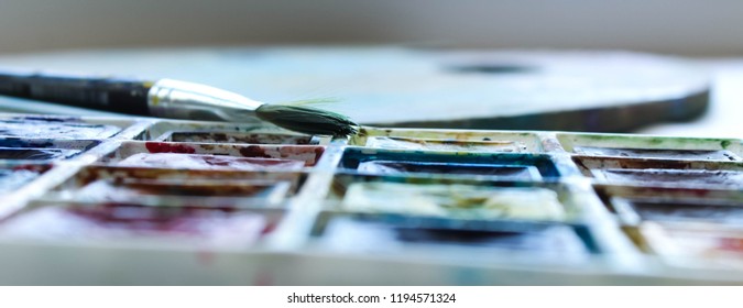 the set of watercolor paints from 20 colors with the brush and the palette in the process of drawing. selective focus