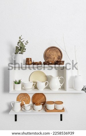 A set of white stylish open shelves with various ceramic white dishes, eco-friendly wooden dishes. white textured wall. kitchen without waste