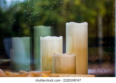 Set Of White Yellow Paraffin Artificial Tall Candles Against Wet Window With Water Droplets, Fall Rain Outside A Window Decor For Cozy Home Comfort. Autumnal Cold Rainy Weather Still Life. Fall Season