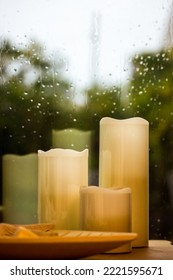 Set Of White Yellow Paraffin Artificial Tall Candles Against Wet Window With Water Droplets, Fall Rain Outside A Window Decor For Cozy Home Comfort. Autumnal Cold Rainy Weather Still Life. Fall Season