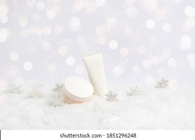 Set Of Winter Skin Care Cosmetic Products In Snow And Snowflakes On White Background With Bokeh Lights. Face Cream Jar And Hand Creme Or Body Lotion Tube. Festive Composition With Copy Space For Text