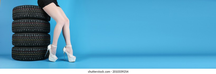  Set Of Winter Studded Wheels And A Female Legs Are On A Blue Background. Winter Tires And Legs Of A Girl Wearing High Heels Are On A Blue Background With Copy Space.