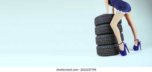 Set Of Winter Studded Wheels And A Woman's Legs Close Up On A Gray Background With Empty Space. Winter Tyres And Legs Of A Lady Wearing High Heels On A Grey Background With Copy Space.