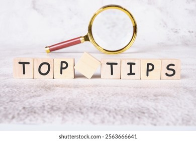 A set of wooden blocks spelling out the words top tips sits on a textured background, accompanied by a magnifying glass, symbolizing clarity in business finance strategies.