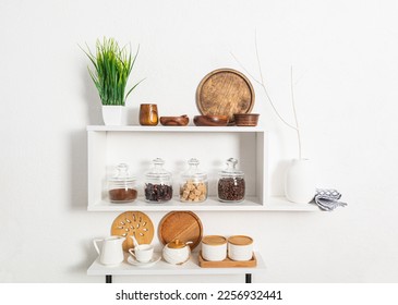 a set of wooden and ceramic dishes, glass filled jars with bulk products on white kitchen shelves on textured wall. compact storage. Stylish design. - Shutterstock ID 2256932441
