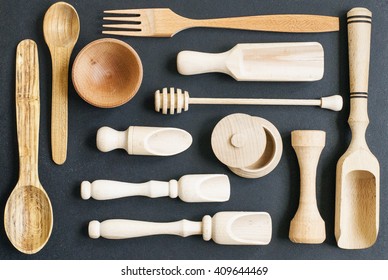 Set Of The Wooden Kitchen Utensils On Black Wooden Background. Spoon, Mortar, Kitchen Spatula, Rolling Pin, Bowl Fork,. Overhead View Of Wood Utensils On Black Wood Board Background.