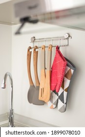 Set Of Wooden Kitchen Utensils And Oven Mitt Hanging On White Wall Over Washing Tap In Small Kitchen.