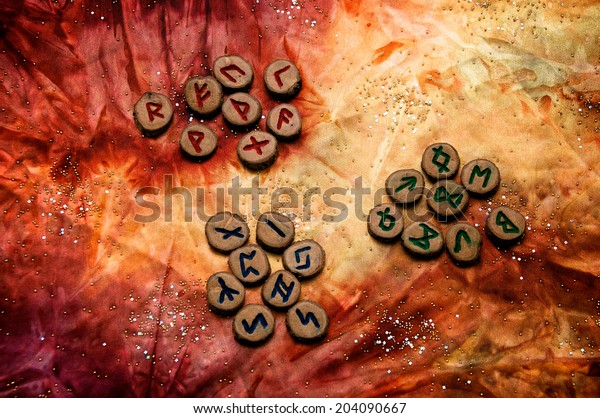 set of wooden runes, an ancient alphabet\
known as the futhark are divided into the three aetts, on a hand\
dyed fabric with small sparkling\
beads.