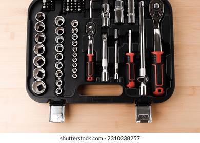 A set of working tools in black plastic bag, a screwdriver, adjustable spanner, sockets for repair on a bamboo, wooden background. Top view