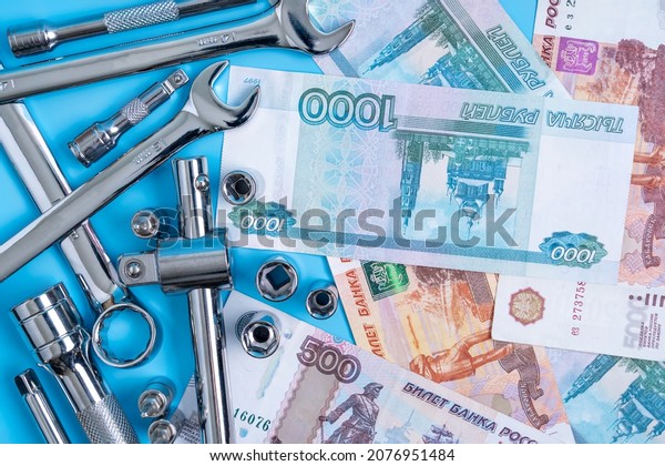 Set of wrenches and other tool for car\
repair, various ruble bills on a blue\
background