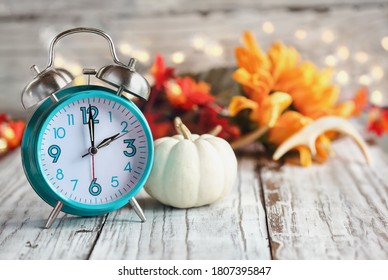 Set your clocks and fall back. Clock and decorations of mini pumpkins, colorful autumn leaves, antlers and bokeh lights over a white wooden table. Daylight saving time concept.  - Shutterstock ID 1807395847