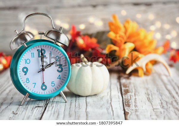 Set your
clocks and fall back. Clock and decorations of mini pumpkins,
colorful autumn leaves, antlers and bokeh lights over a white
wooden table. Daylight saving time concept.
