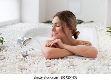 Set your mind at ease! Beautiful smiling young lady posing for camera, while lying in the hot bath with bubbles and having a great spare time.