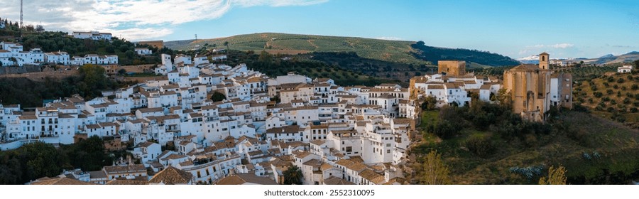 Setenil de las Bodegas in Spain features houses built into cliffs, whitewashed buildings, terracotta roofs, and a large church amidst rolling hills. - Powered by Shutterstock