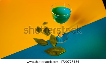 Setting of alcoholic beverage on multi-colored background. Stock footage. Blue alcoholic drink stands on decorative colorful background with green leaves adorning background