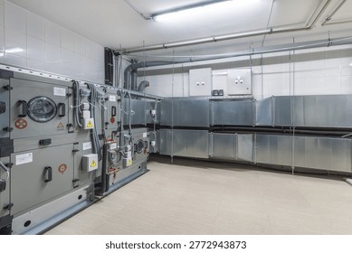 The setting features a large ventilation system installed in an industrial building. The area is bright with metal equipment arranged along the walls and pipes above.