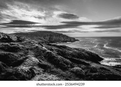 The setting features a striking black and white coastal landscape, highlighting rugged cliffs and the turbulent ocean under a dramatic sky at dusk. - Powered by Shutterstock