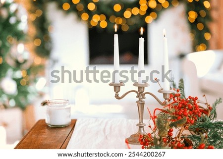 The setting features a stylish table adorned with silver candle holders, white candles, and vibrant holiday decorations, creating a warm and inviting atmosphere during the festive season.