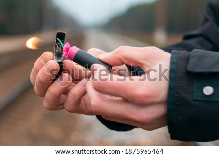 Setting Fire to the Firecracker. Man in Black Clothes Lighting Up the Petard. Firing Up the Pyrotechnics with a Black Gasoline Lighter Outdoors