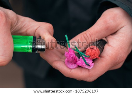Setting Fire to the several Firecrackers. Man in Black Clothes Lighting Up Two Petards at the Same Time. Firing Up the Pyrotechnic with Green Gas Lighter Outdoors
