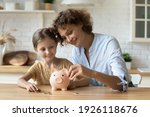 Setting good example. Young parent mother teach child little daughter girl to manage finances save money spend earnings with economy plan family budget. Friendly mom and kid thrift coins in piggybank