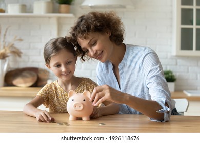 Setting good example. Young parent mother teach child little daughter girl to manage finances save money spend earnings with economy plan family budget. Friendly mom and kid thrift coins in piggybank - Shutterstock ID 1926118676