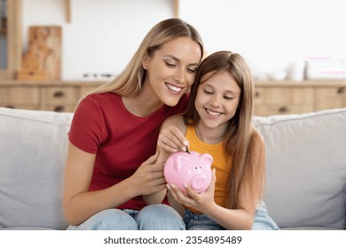Setting good example. Young parent mother teach child little daughter girl to manage finances save money spend earnings with economy plan family budget. Friendly mom and kid thrift coins in piggybank