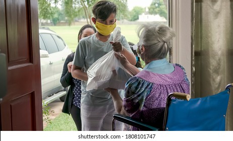 Setting a great example this mother who is part of a volunteer food delivery program takes her children along with her to deliver food to an elderly woman in a wheelchair. - Shutterstock ID 1808101747