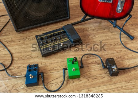 Setting up guitar audio processing effects. Electric guitar stomp box effectors and cables on studio floor next to guitar amp and guitar.