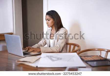 Setting up her own design website. A young woman typing on her laptop while sketches and pencils lie next to her on the desk.