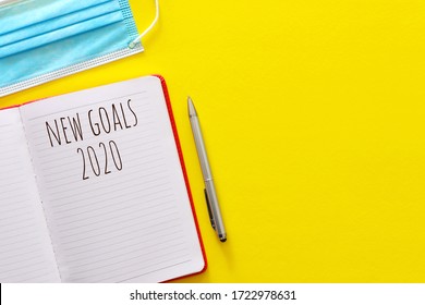 Setting New Goals List In 2020 Due To Corona Virus Covid-19 Outbreak. Business Concept Of Top View With Notebook, Cup Of Coffee Over Yellow Desk