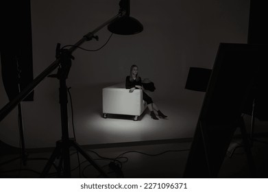 Setting up the photo session behind the scenes: the girl is preparing for the photo shoot, sitting on the sofa, around the camera equipment. Fashion Magazine studio photo session, directed light, low  - Powered by Shutterstock